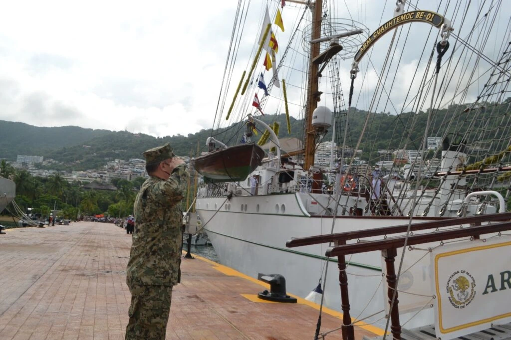 ARM Cuauhtémoc atracado en puerto mientras un elemento uniformado saluda frente a la embarcación.