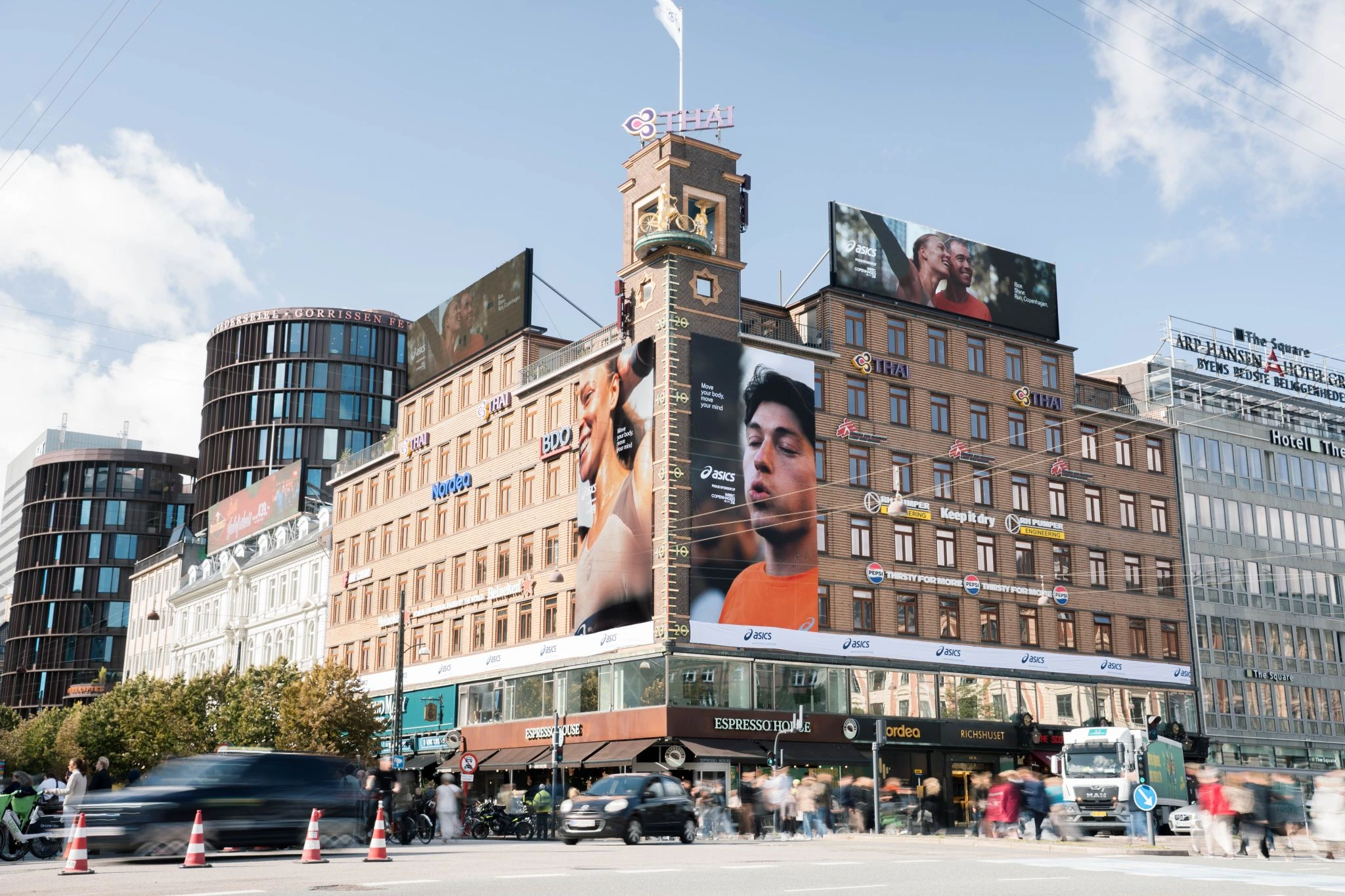 Campaña OOH de ASICS en Copenhague con varios billboards de gran formato instalados sobre edificios en una zona urbana de alto tráfico.