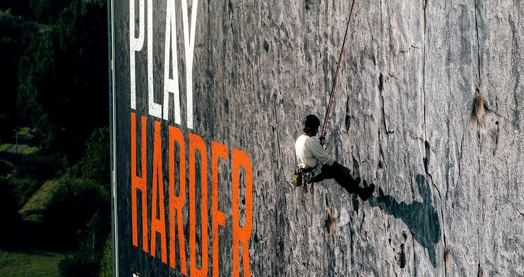 Escalador subiendo la superficie de un billboard Garmin Play Harder como parte de una activación OOH experiencial.