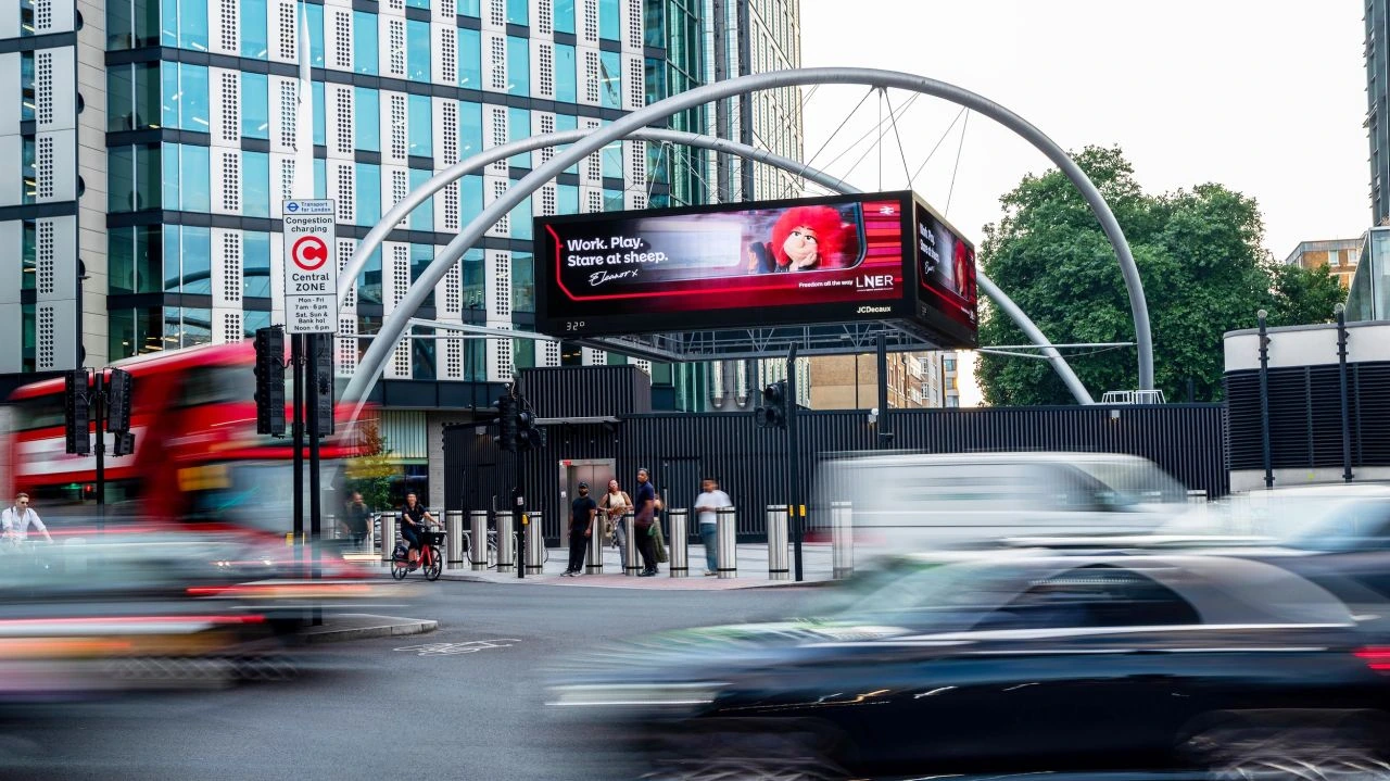 Billboard digital de LNER en Londres con Eleanor y el mensaje Work. Play. Stare at sheep.