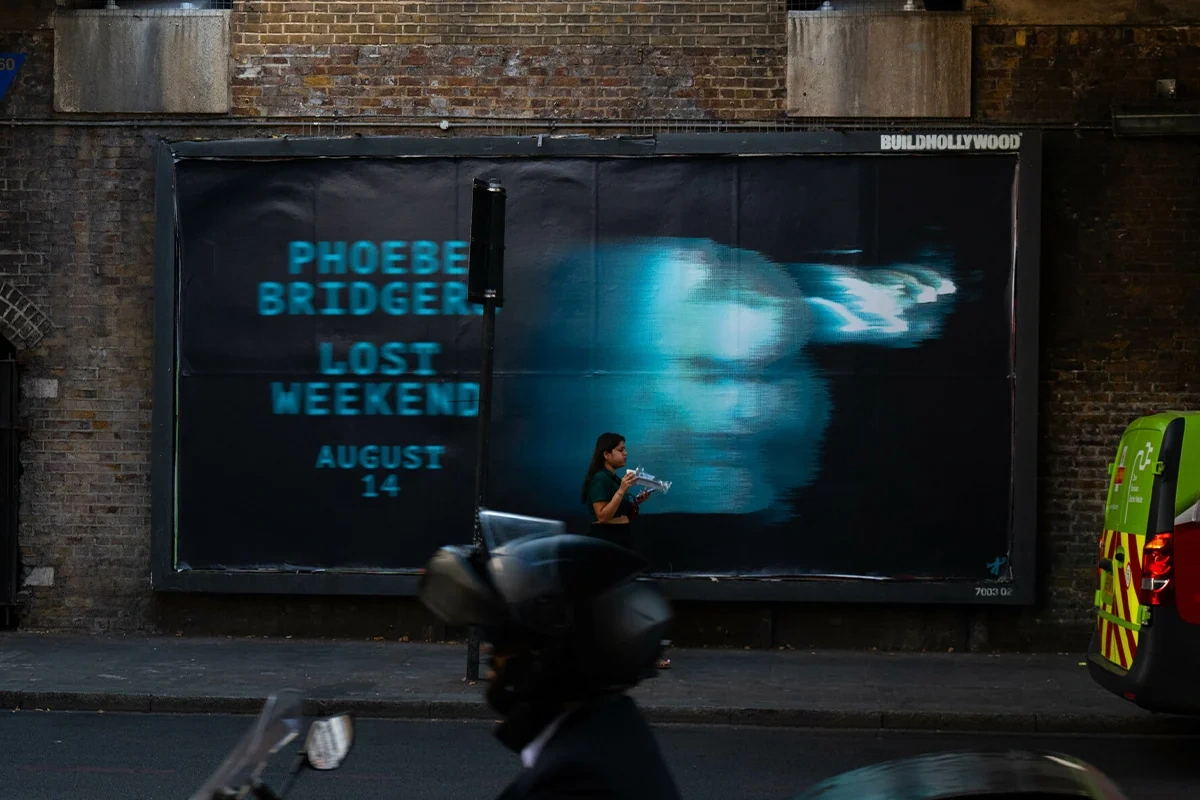 Billboard urbano de Phoebe Bridgers para Lost Weekend con imagen azul distorsionada, nombre de la artista y fecha de lanzamiento.